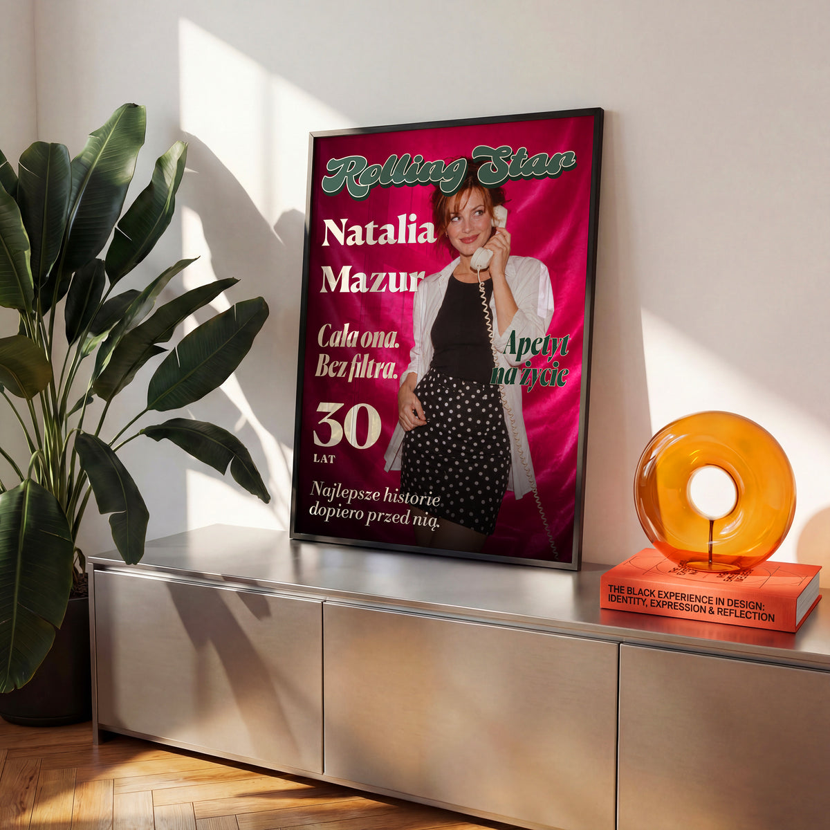 Personalizowany plakat Rolling Star w czarnej ramce na komodzie. Różowa satyna i litery retro tworzą osobistą okładkę ze zdjęciem.