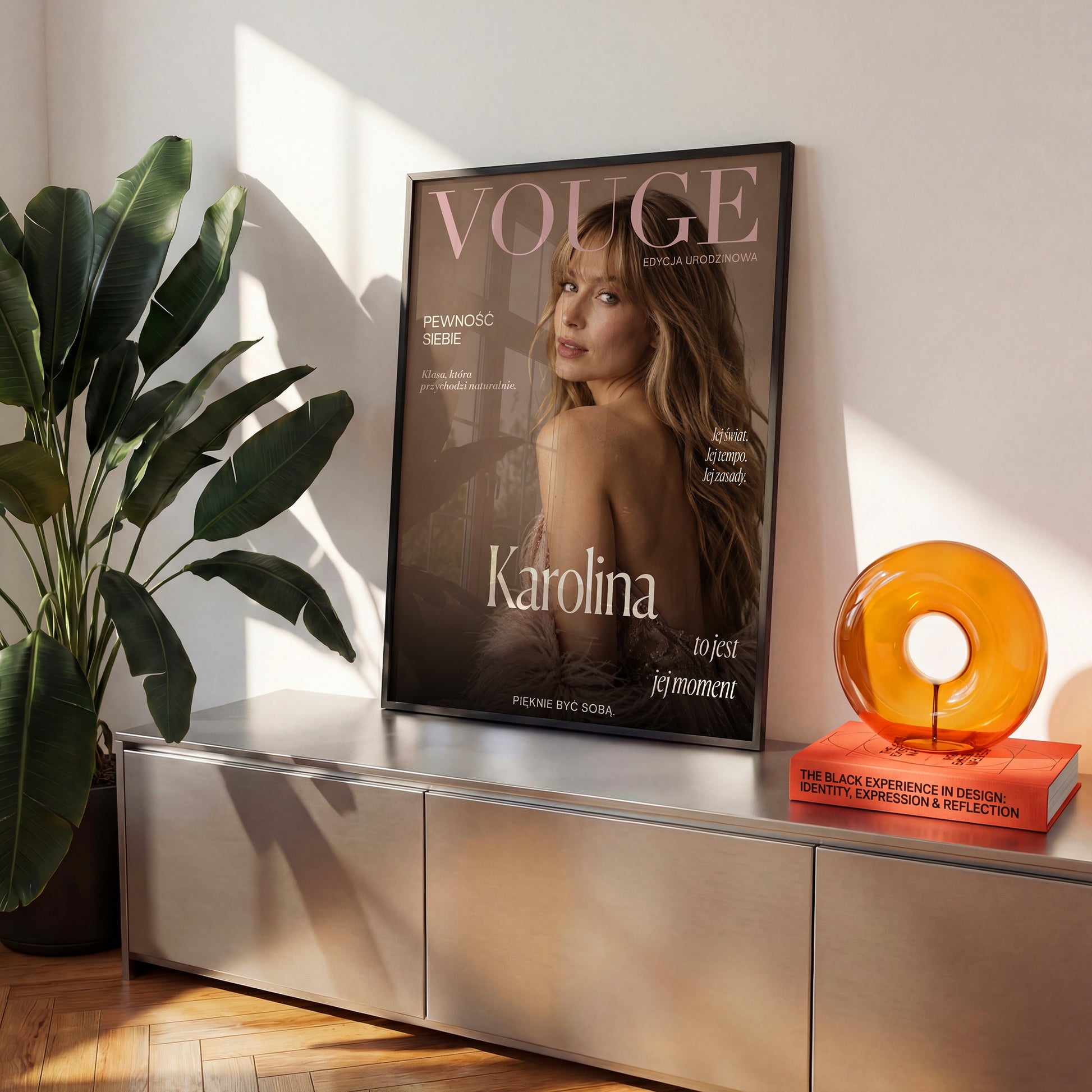 Personalizowany plakat Vouge Jej Moment w czarnej ramce na komodzie. Pudrowe litery na ciepłym tle taupe tworzą osobistą okładkę ze zdjęciem.