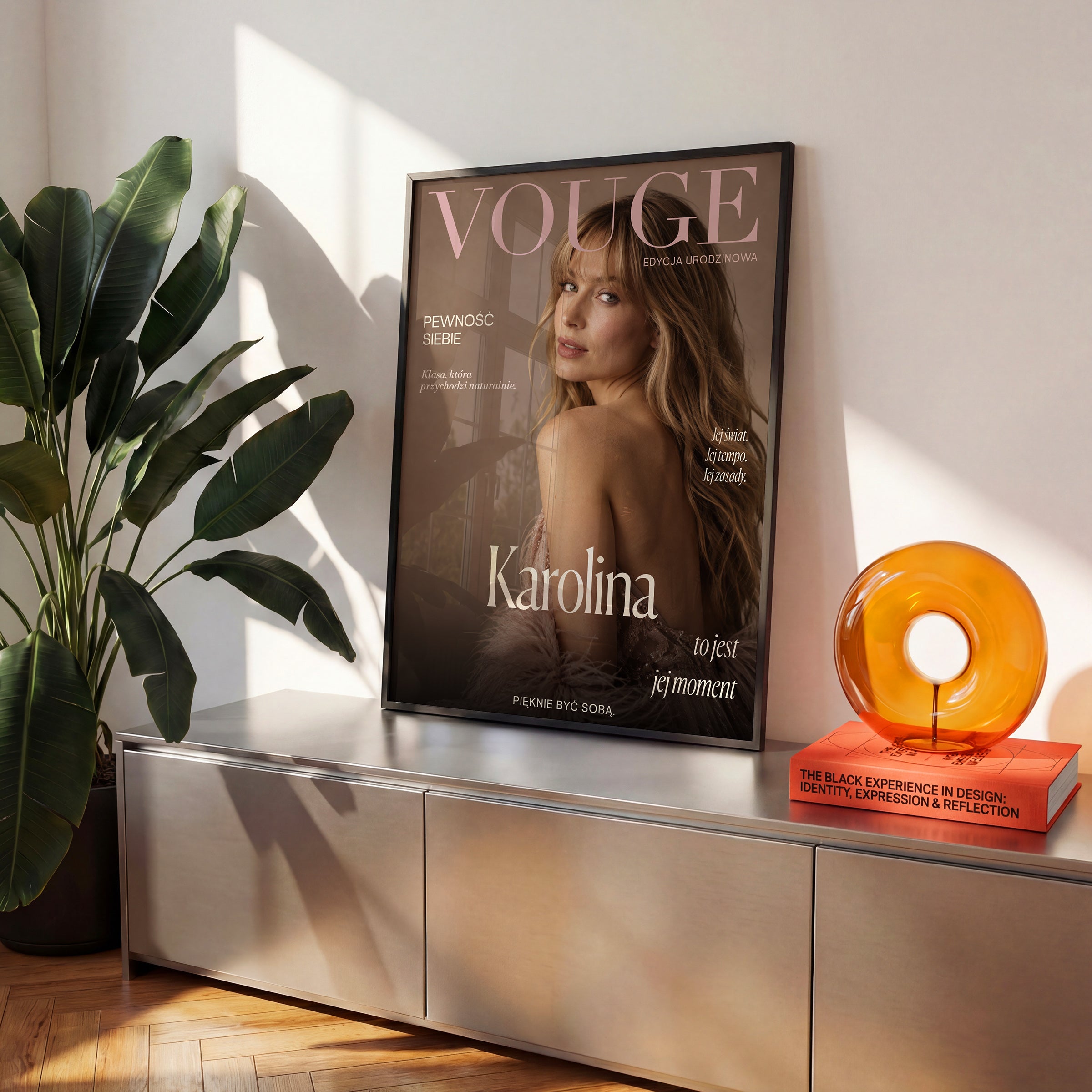 Personalizowany plakat Vouge Jej Moment w czarnej ramce na komodzie. Pudrowe litery na ciepłym tle taupe tworzą osobistą okładkę ze zdjęciem.