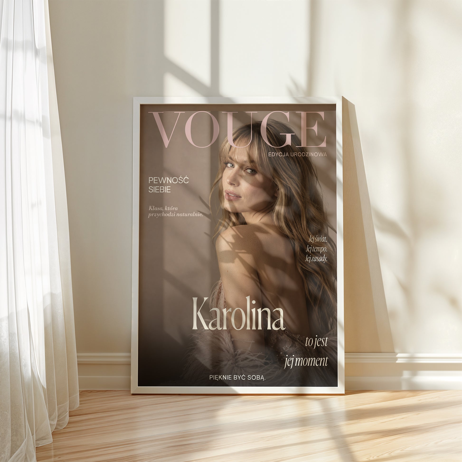 Personalizowany plakat Vouge Jej Moment w białej ramce przy oknie. Pudrowe litery na ciepłym tle taupe tworzą osobistą okładkę ze zdjęciem.