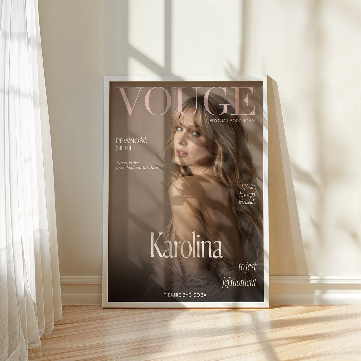 Personalizowany plakat Vouge Jej Moment w białej ramce przy oknie. Pudrowe litery na ciepłym tle taupe tworzą osobistą okładkę ze zdjęciem.