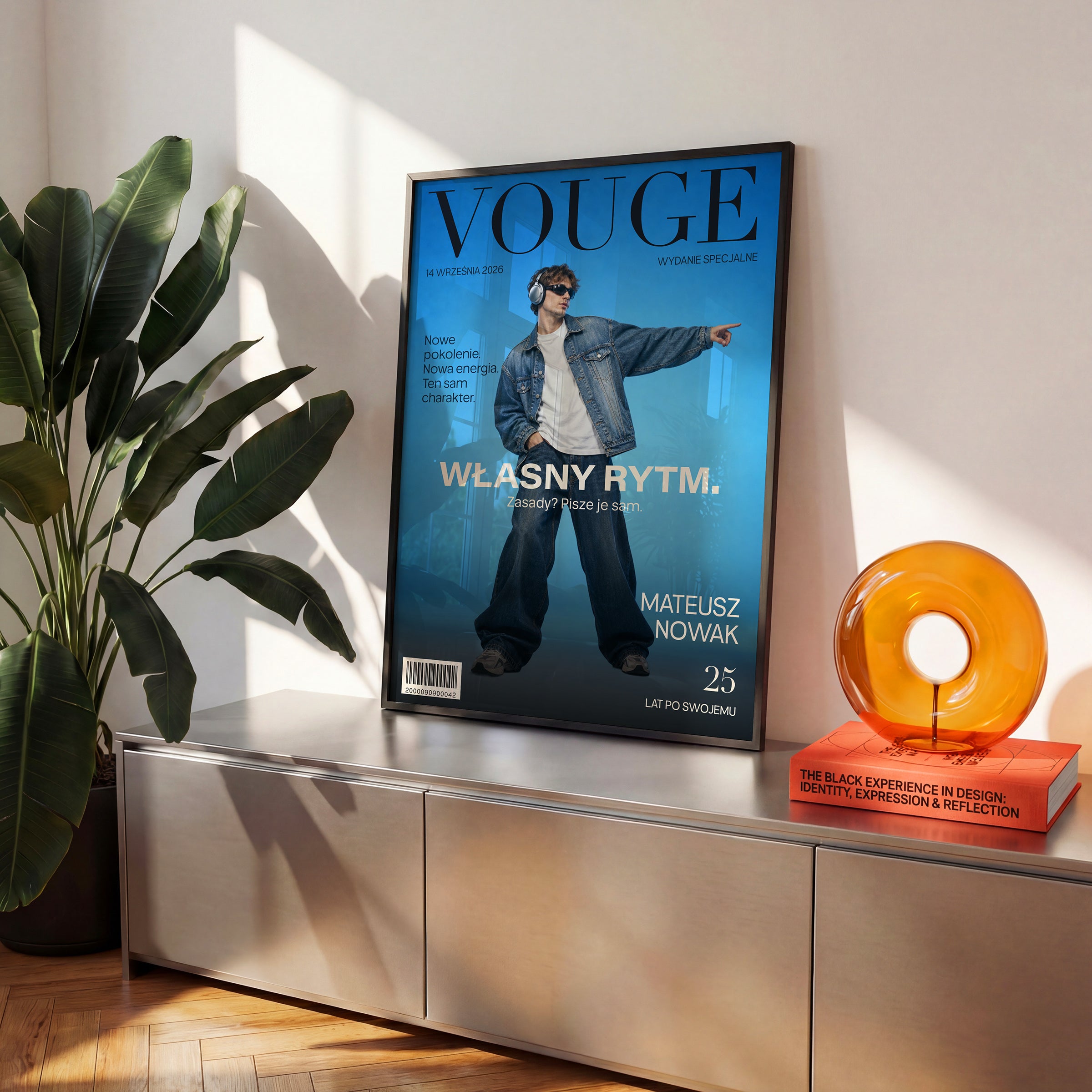 Personalizowany plakat Vouge Własny Rytm w czarnej ramce na komodzie. Niebieskie tło i szerokie jasne hasło tworzą osobistą okładkę ze zdjęciem.