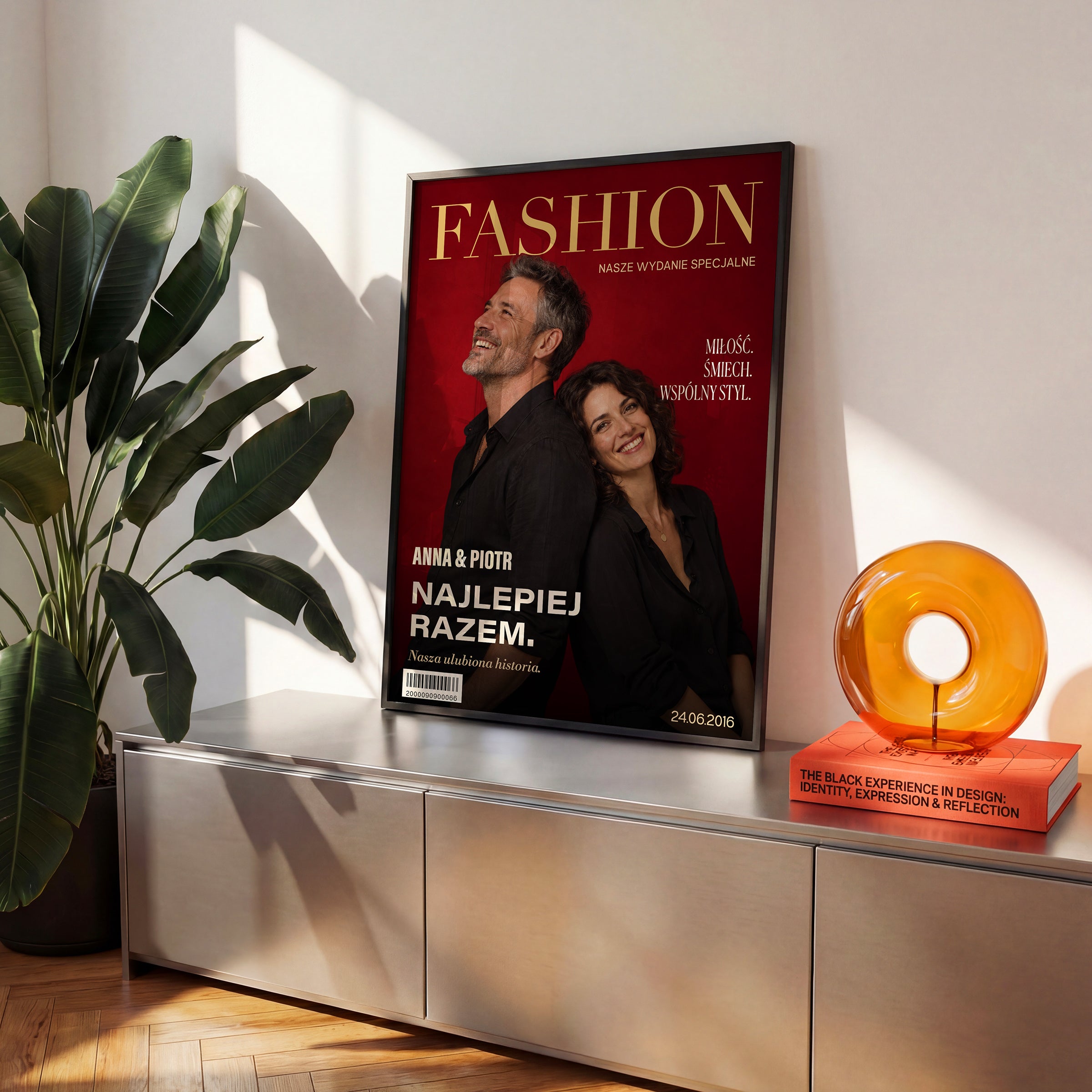 Personalizowany plakat Fashion Dla Pary w czarnej ramce na komodzie. Czerwone tło, złocisty tytuł i wspólny portret tworzą osobistą okładkę ze zdjęciem.
