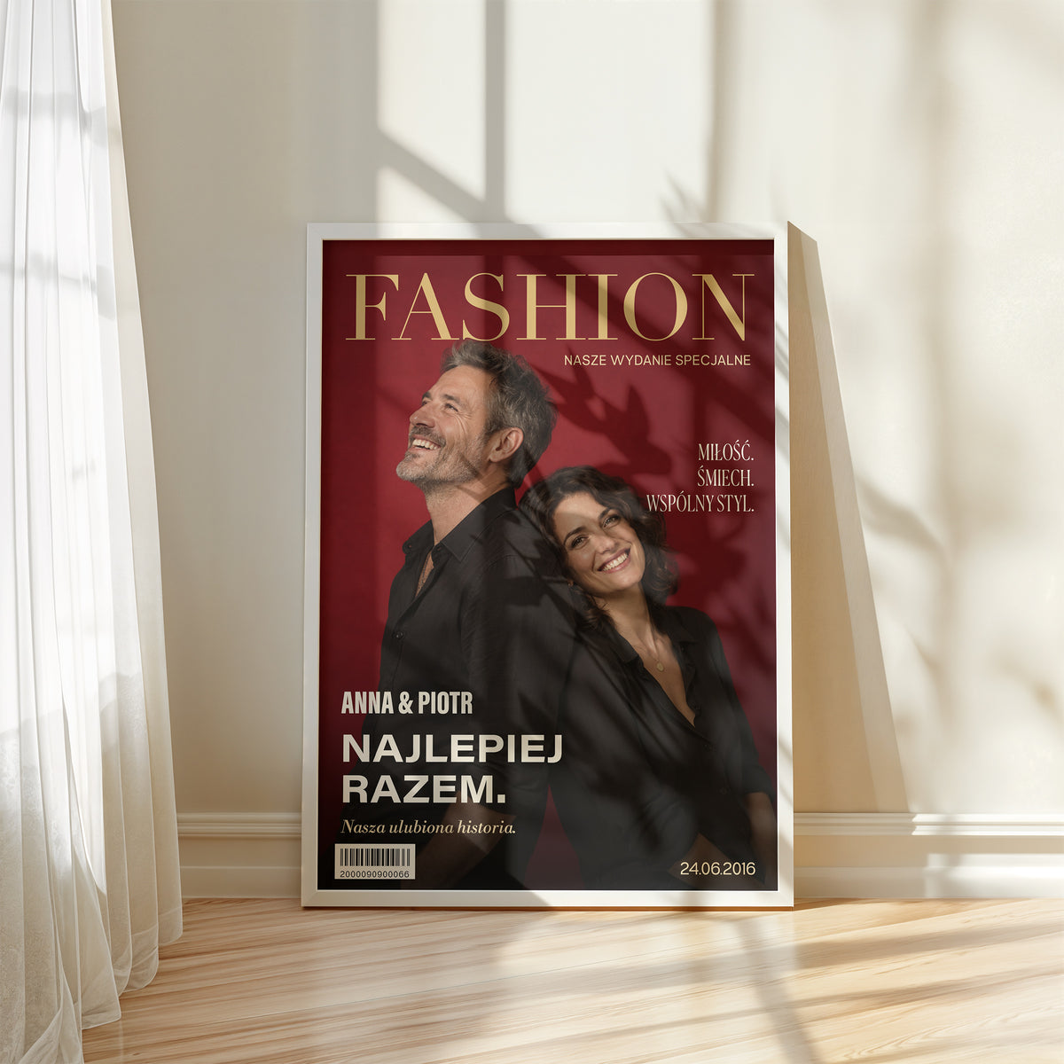 Personalizowany plakat Fashion Dla Pary w białej ramce przy oknie. Czerwone tło, złocisty tytuł i wspólny portret tworzą osobistą okładkę ze zdjęciem.