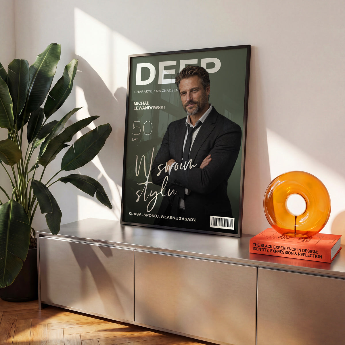 Personalizowany plakat DEEP — W SWOIM STYLU w czarnej ramce ustawiony na komodzie, z własnym portretem, imieniem i napisami na okładce magazynu.