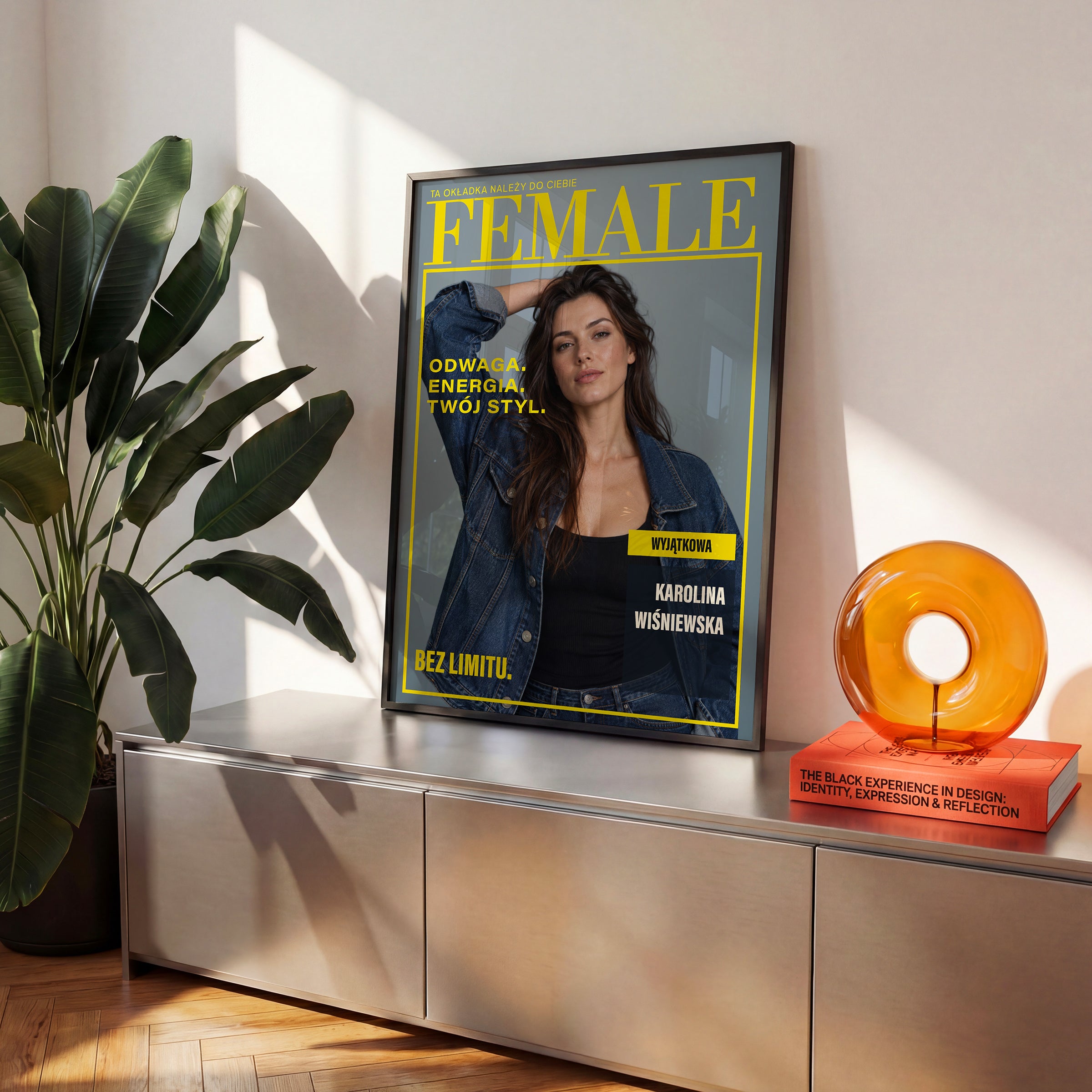 Personalizowany plakat FEMALE — ENERGIA BEZ LIMITU w czarnej ramce ustawiony na komodzie, z własnym portretem, imieniem i napisami na okładce magazynu.