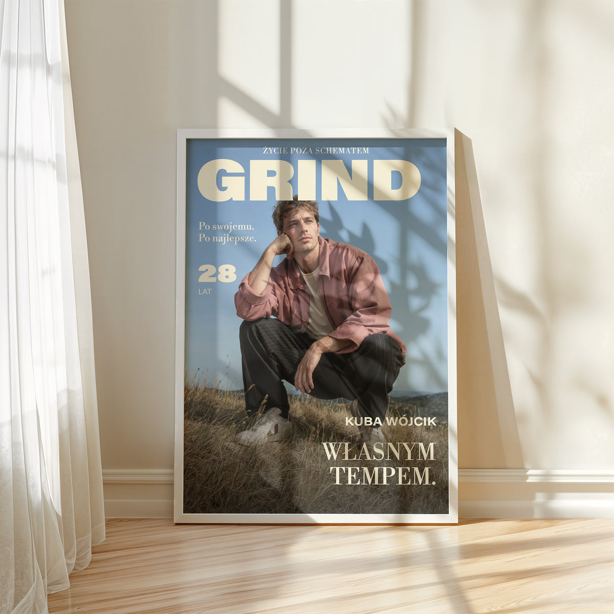 Personalizowany plakat GRIND — WŁASNYM TEMPEM w białej ramce przy oknie, z własnym portretem, imieniem i napisami na okładce magazynu.