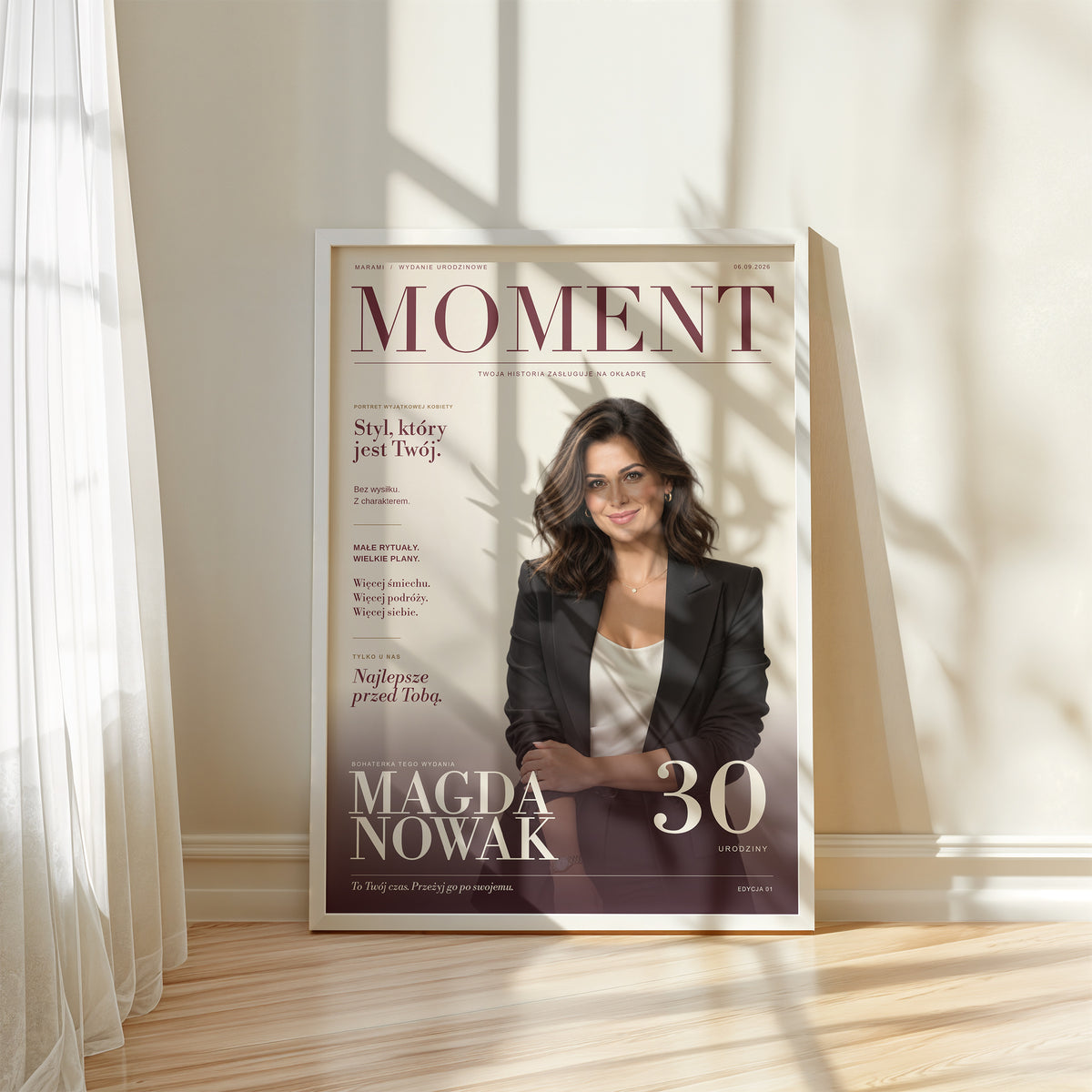 Personalizowany plakat MOMENT w białej ramce przy oknie, w naturalnym świetle. C-PL-COVMAG-3-2130-NF