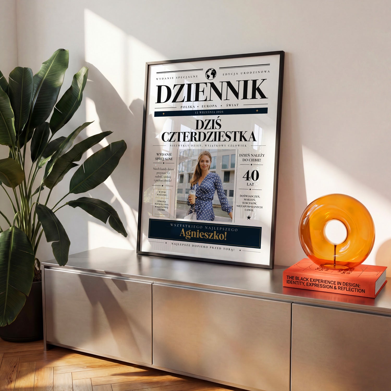 Plakat urodzinowy w stylu gazety dziennik w czarnej ramce na metalowej komodzie w jasnym salonie
