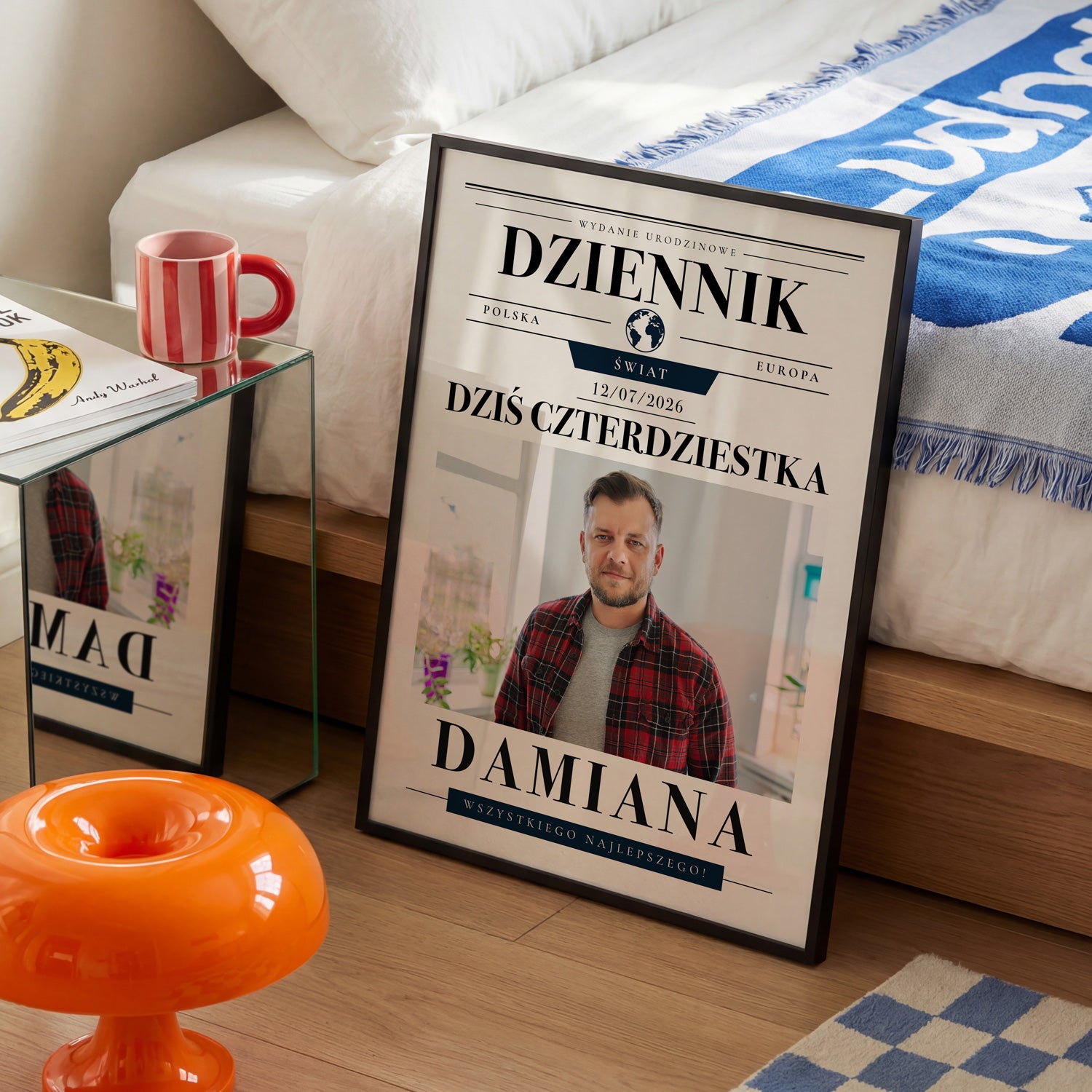Plakat urodzinowy dziennik w czarnej ramce ustawiony w sypialni obok łóżka i czerwonego kubka