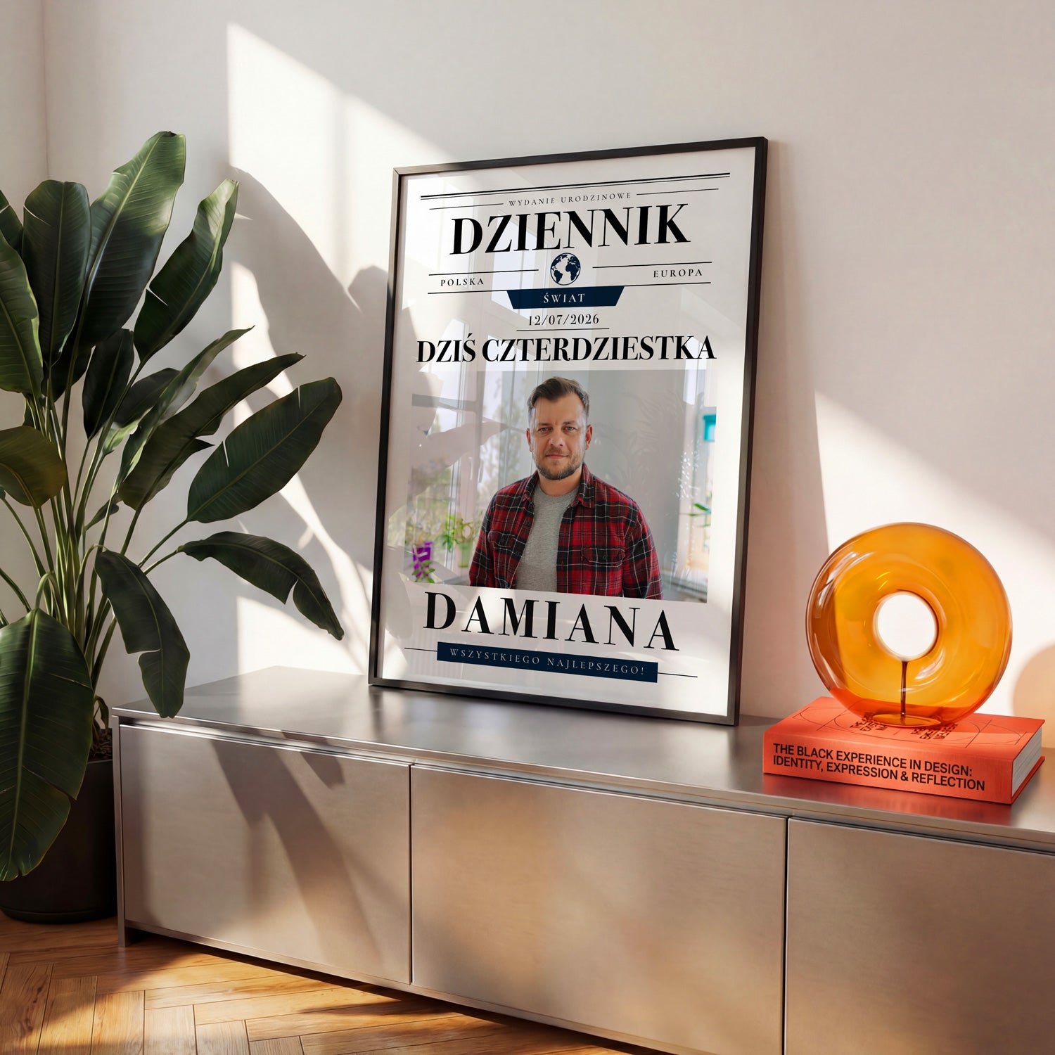 Plakat urodzinowy w stylu gazety dziennik w czarnej ramce na metalowej komodzie w jasnym salonie