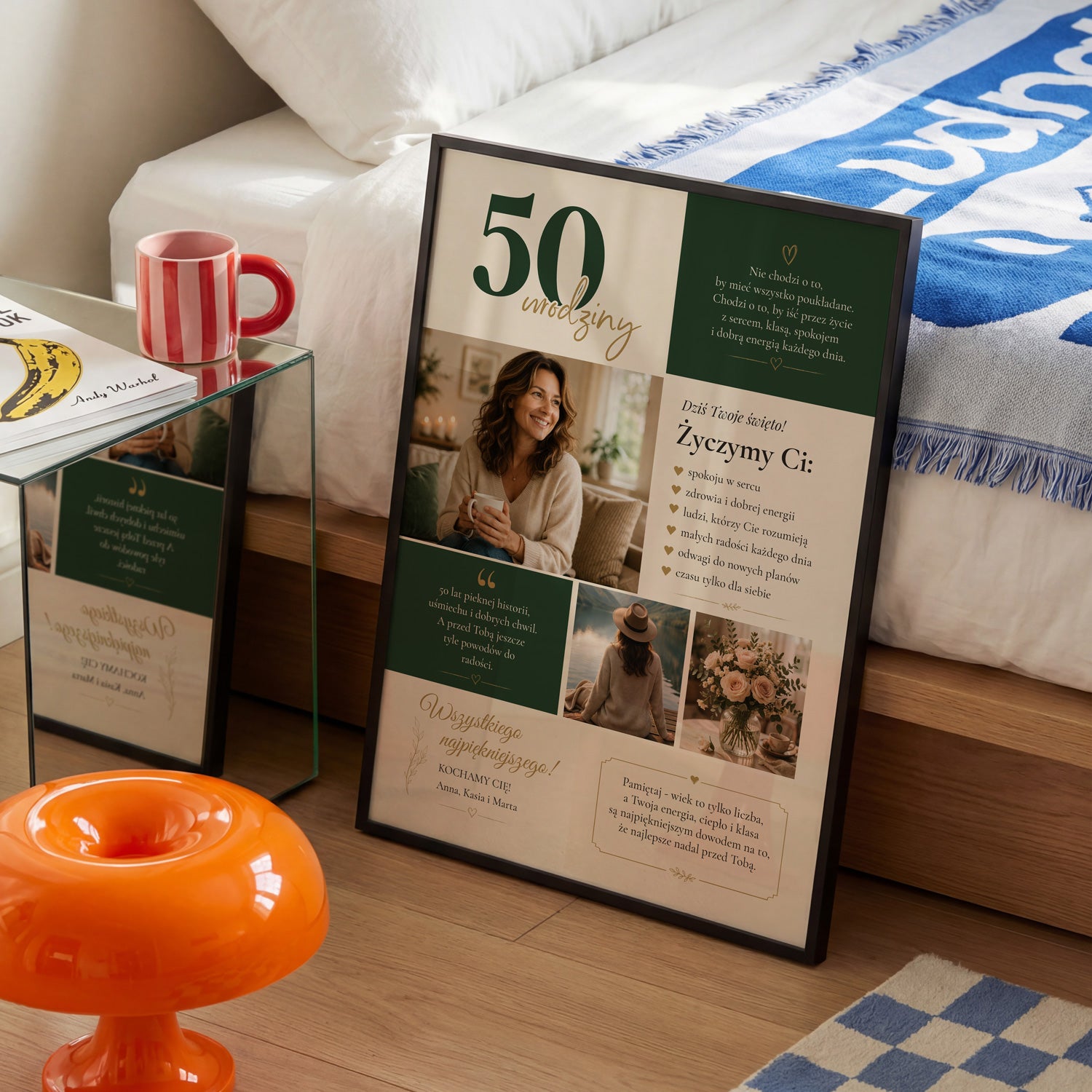Personalizowany plakat na 50 urodziny dla niej z życzeniami i zdjęciami w czarnej ramce, ustawiony w sypialni obok łóżka i czerwonego kubka