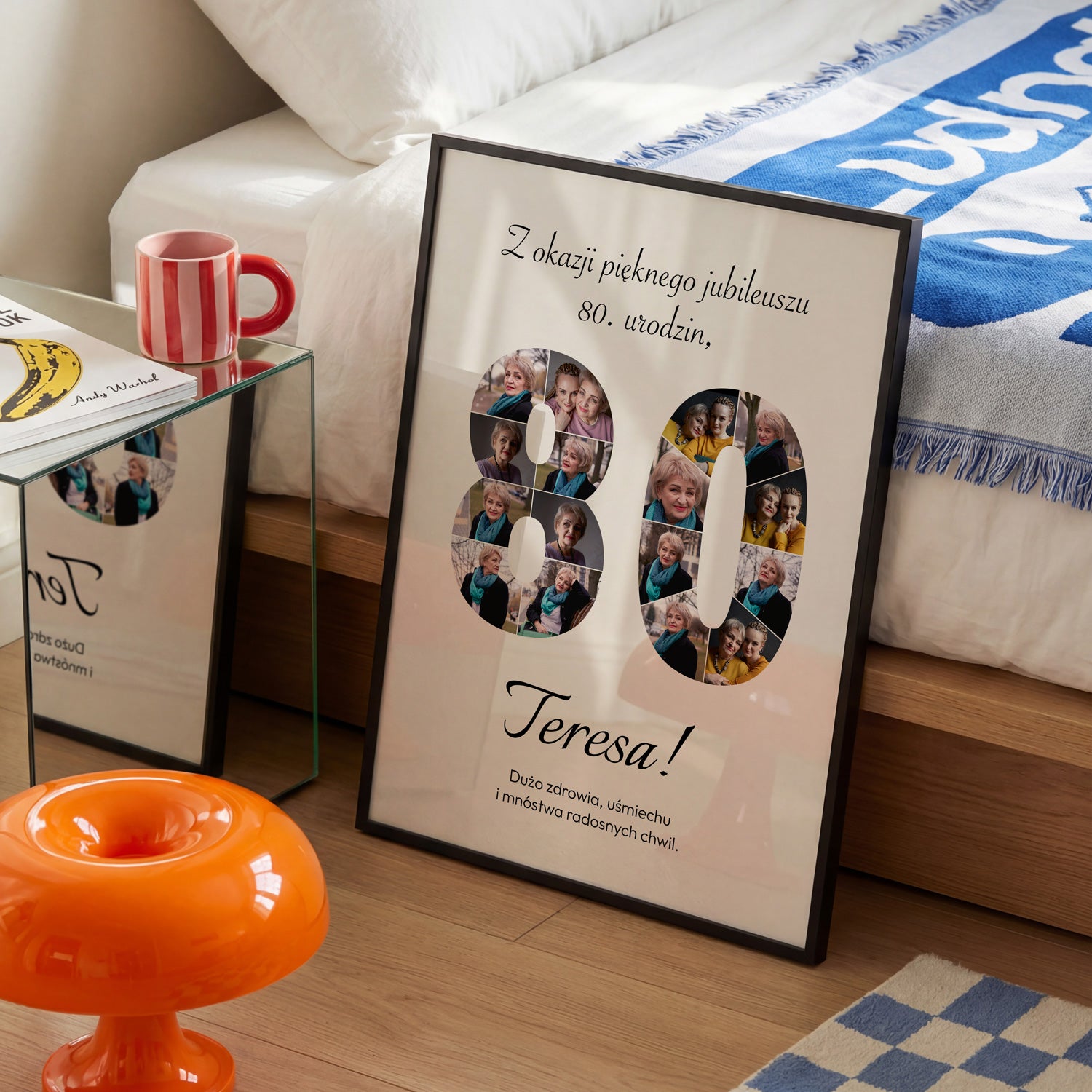 Plakat na 80 urodziny w czarnej ramce z kolażem 16 zdjęć w kształcie cyfry 80 i imieniem Teresa obok łóżka z niebieską narzutą