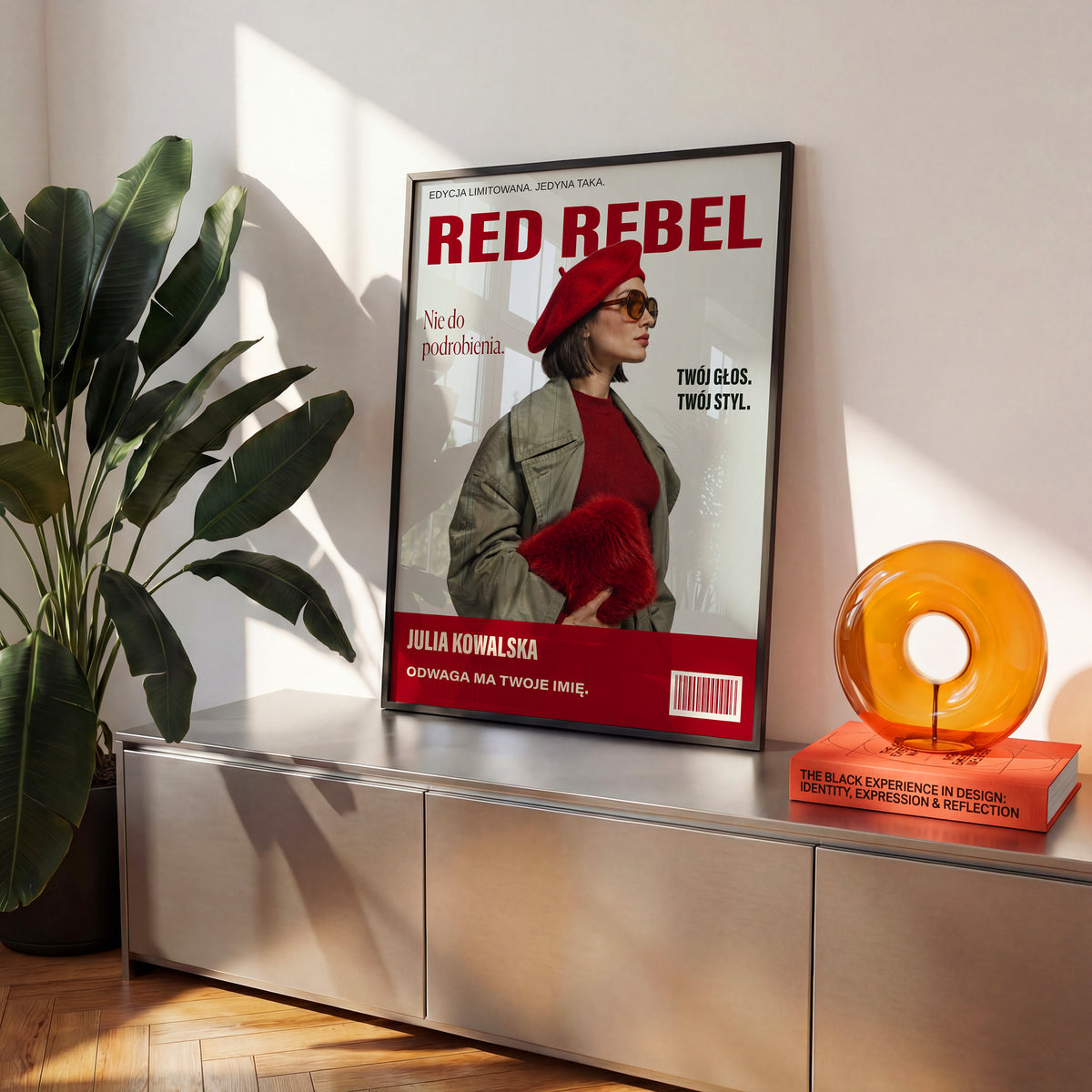 Personalizowany plakat RED REBEL — NIE DO PODROBIENIA w czarnej ramce ustawiony na komodzie, z własnym portretem, imieniem i napisami na okładce magazynu.