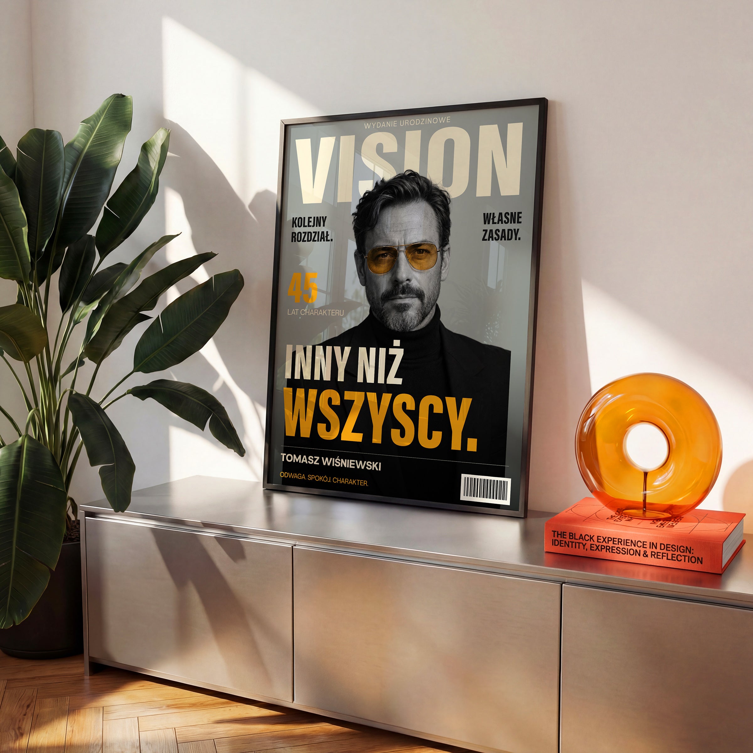 Personalizowany plakat VISION — WŁASNE ZASADY w czarnej ramce ustawiony na komodzie, z własnym portretem, imieniem i napisami na okładce magazynu.