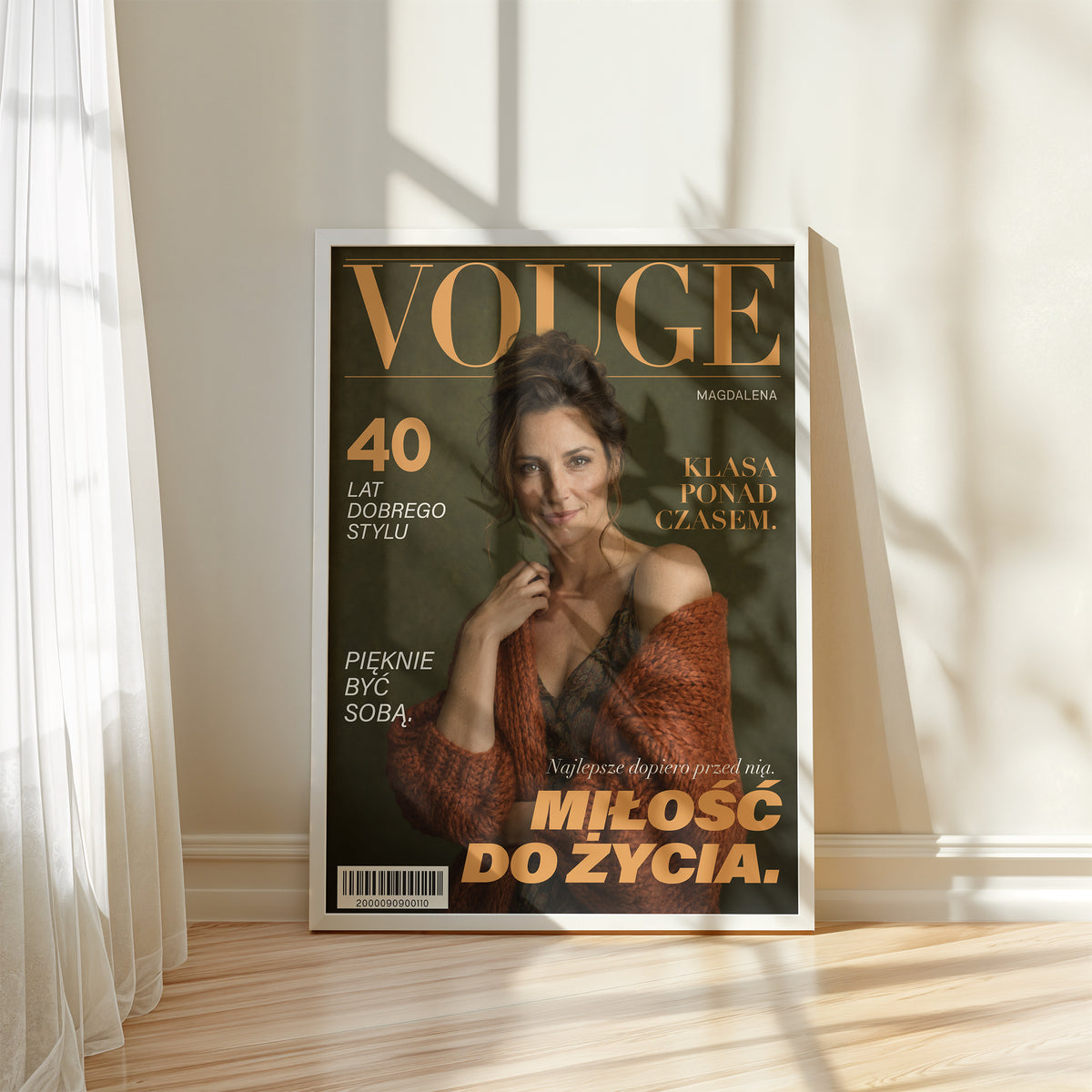 Personalizowany plakat Vouge Ponadczasowa w białej ramce przy oknie. Oliwkowe tło i bursztynowe litery na modowej okładce portretowej.