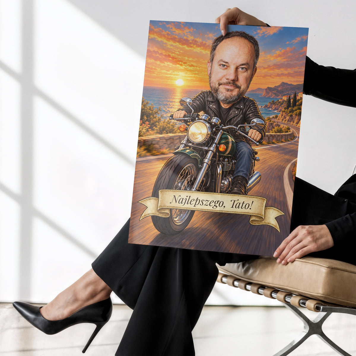 Motocyklista — plakat bez ramki trzymany w dłoniach, z karykaturą mężczyzny na motocyklu, na nadmorskiej drodze o zachodzie słońca. C-PL-KAR-06-2130-NF